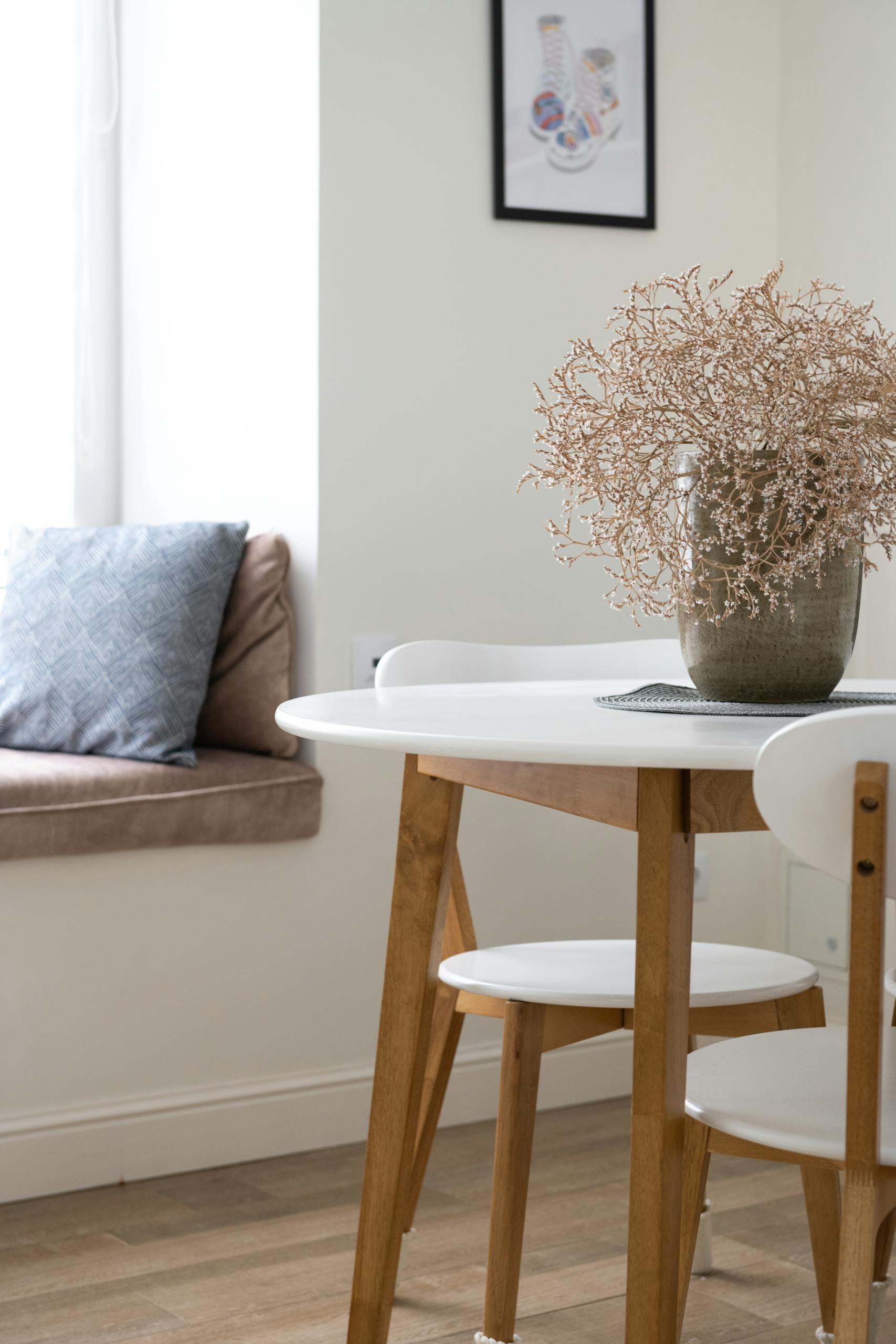 Chairs at table with decorative dried flowers placed in stylish room with picture on wall and cushions on windowsill at home